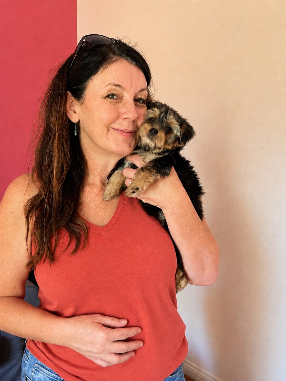 Sheryl Grant, a woman with long dark hair in a rust-colored top, holding a small terrier puppy